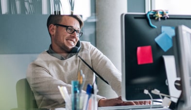 Man answering desk phone while working on desktop